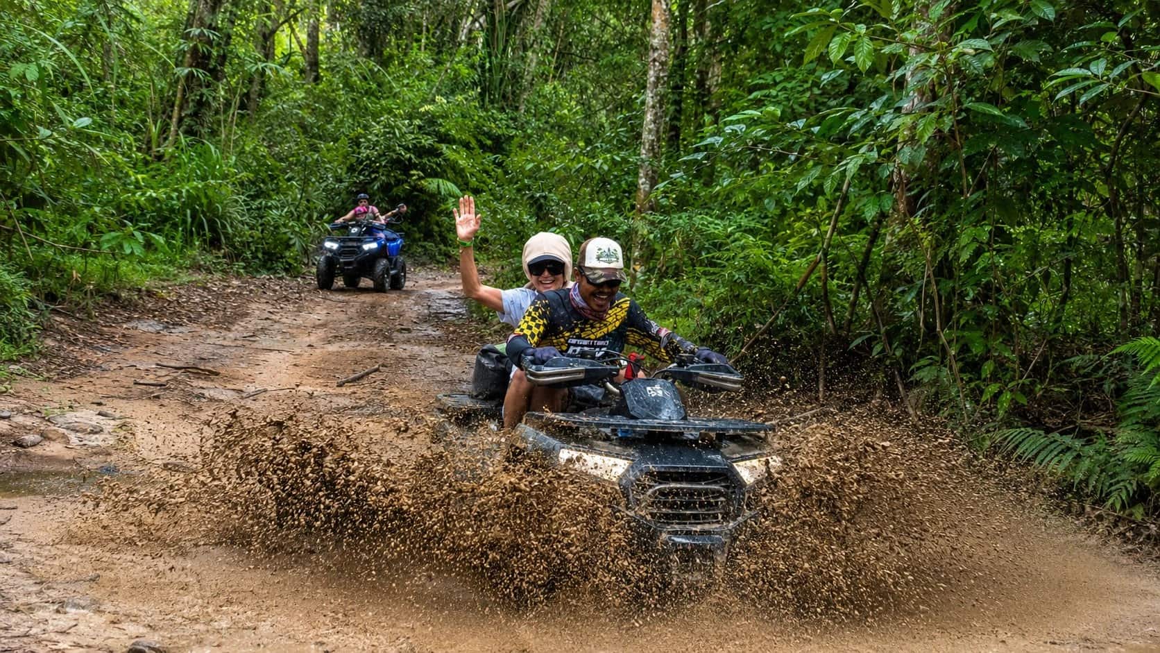 Quad bike splashing through a jungle mud track, guide and passenger waving, Jungle Quad, Koh Samui ATV tours
